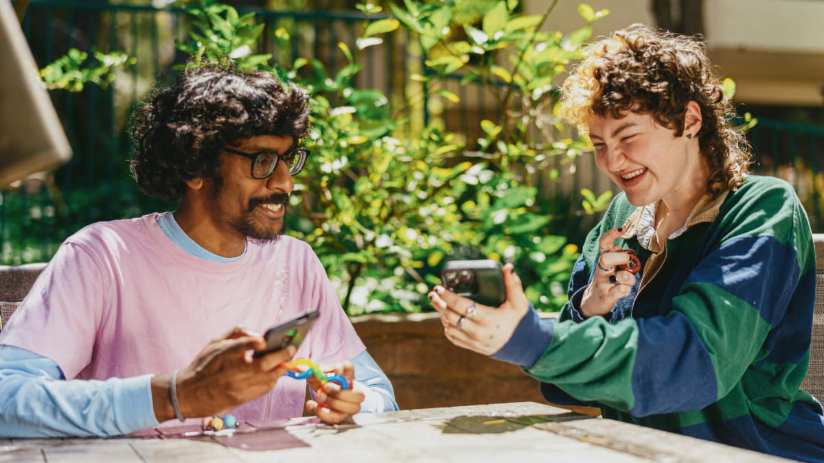 Zwei Menschen sitzen an einem Tisch und halten ein Smartphone und Stimming Toys