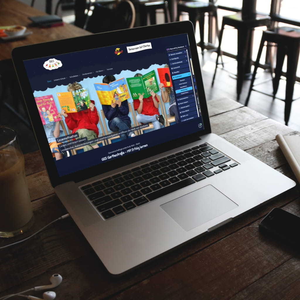 Auf einem Laptop in einem Café ist die Webseite der GGS Garthestraße zu sehen, in welcher der NeuroA11y Assistenten benutzt wird