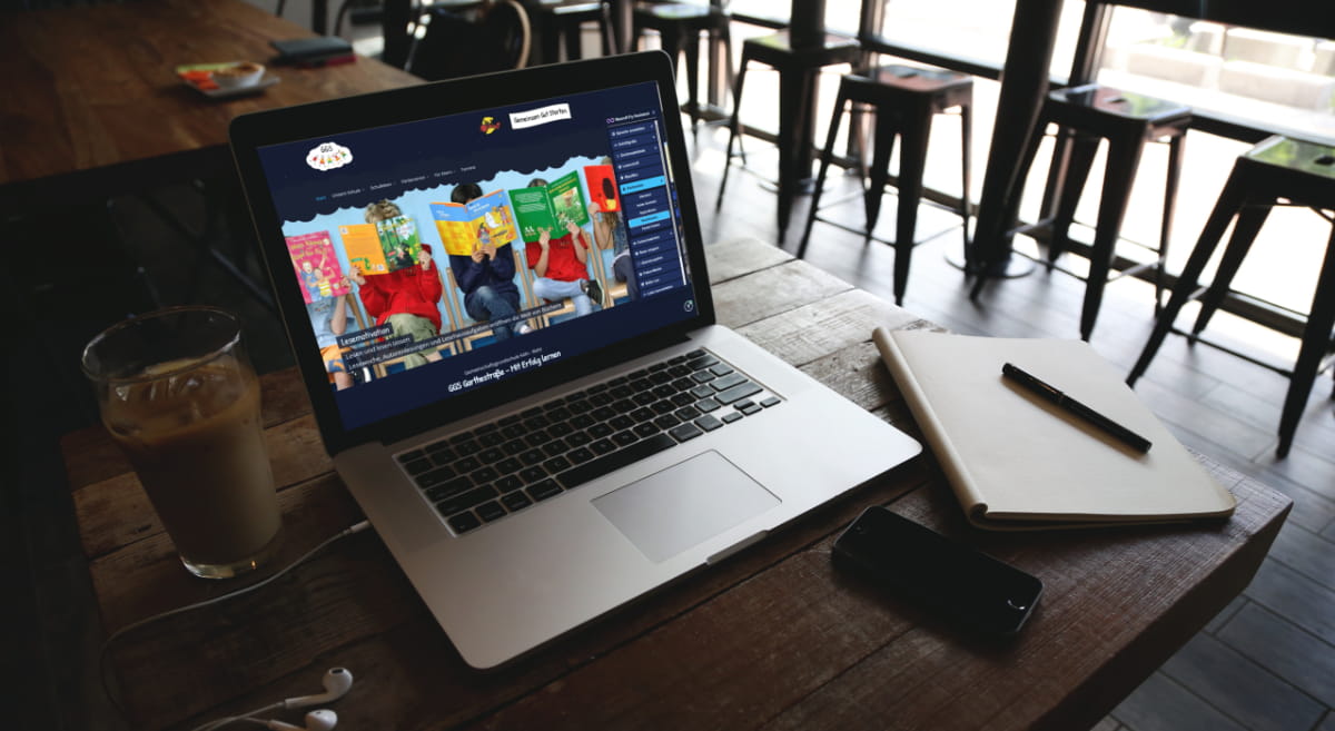 Auf einem Laptop in einem Caf&eacute; ist die Webseite der GGS Garthestra&szlig;e zu sehen, in welcher der NeuroA11y Assistenten benutzt wird